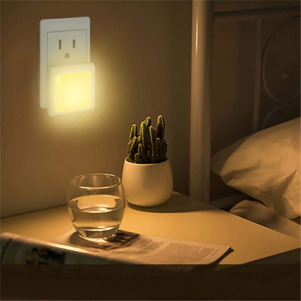 An LED night light plugged in next to a bedside table