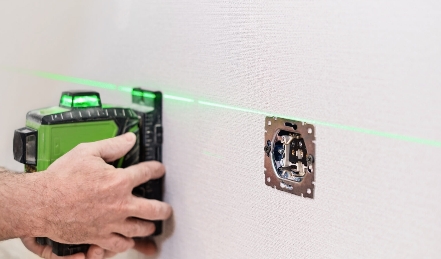 An electrician installs sockets in the apartment. Checking the installed sockets on the wall of the apartment with a laser level, selective focus on the sockets