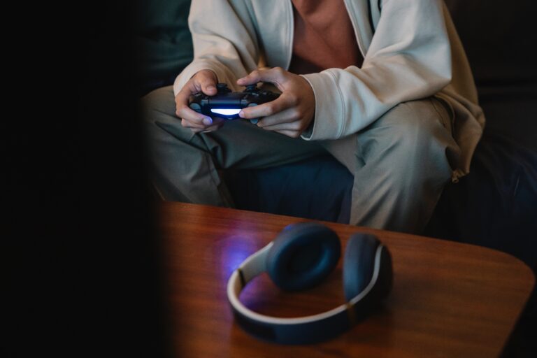 A man holding a PS4 controller with wireless headphones on a table next to him