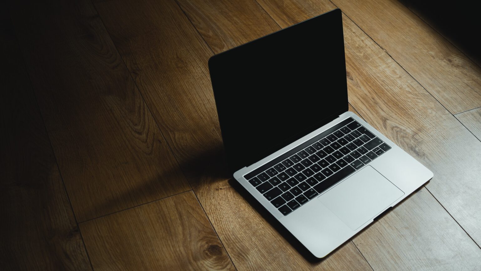 A MacBook Pro with a black screen on wooden flooring