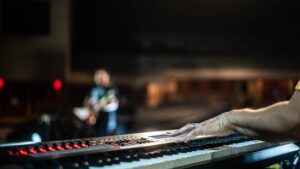 A hand on a digital piano with a blurred hall in the background