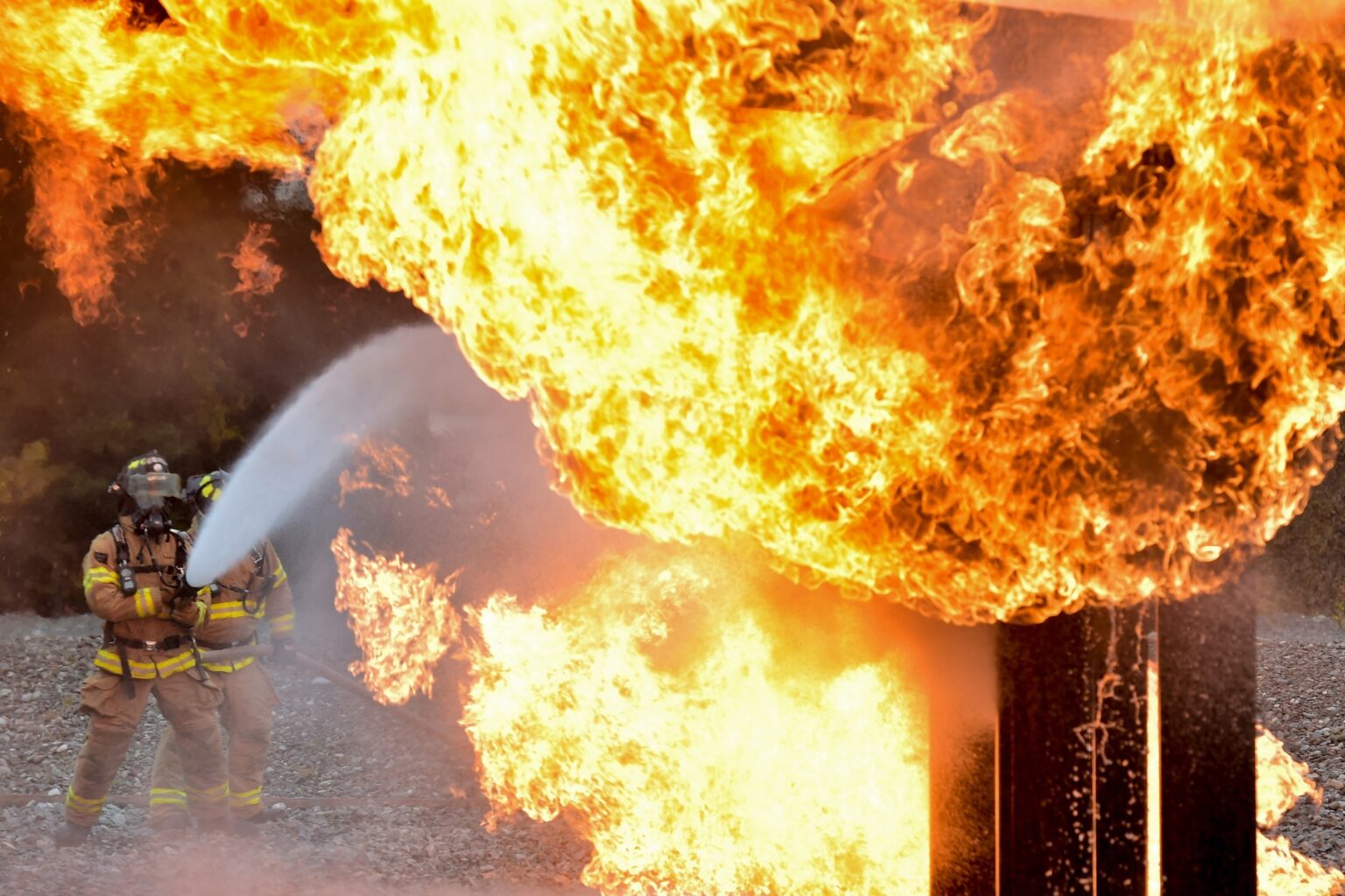 Two fireman using a hose to put out a large fire