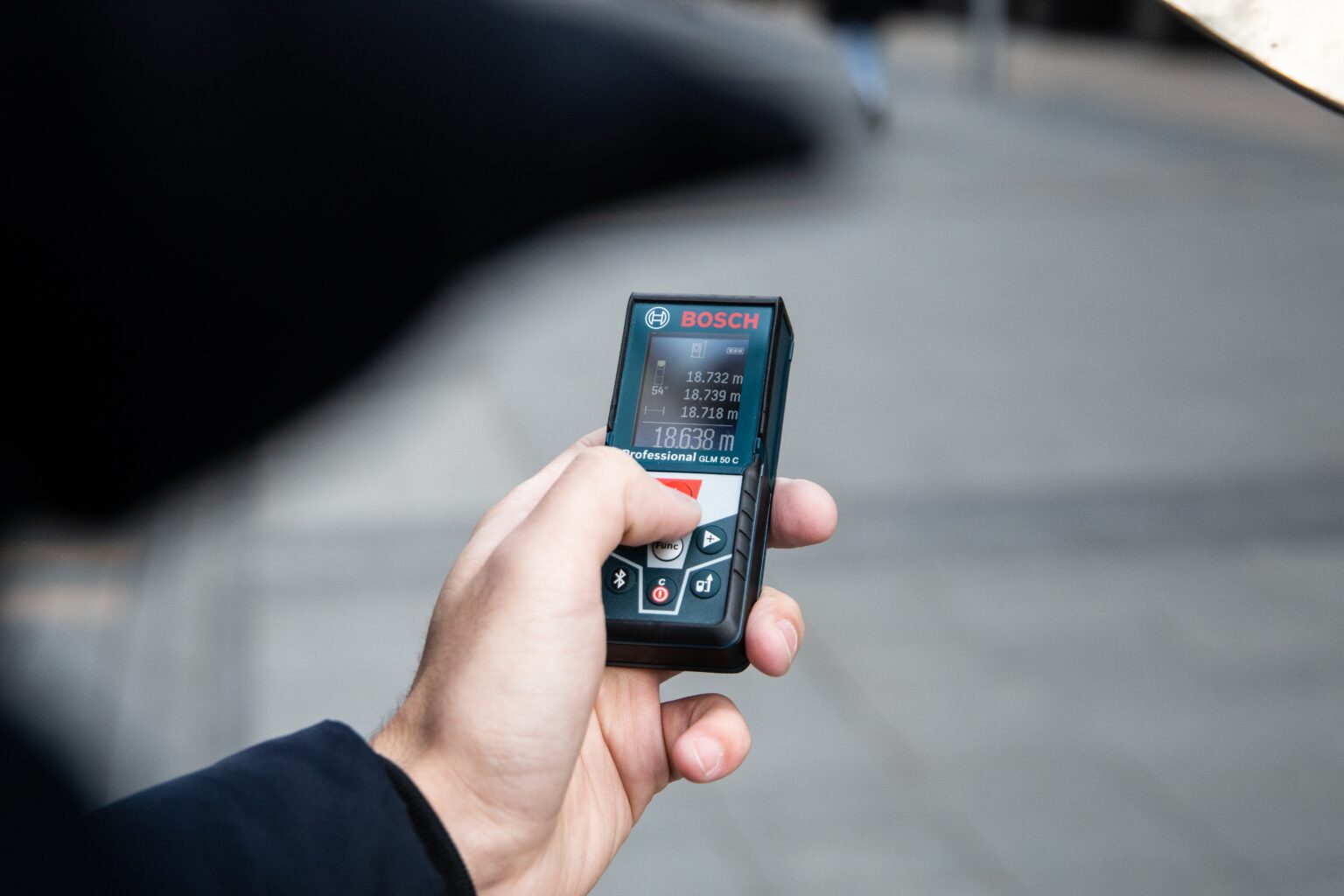 A hand holding a Bosch Laser Measure with a blurred grey background