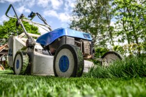 A closeup of an Electric Lawn Mower cutting grass with trees and the sky in the background