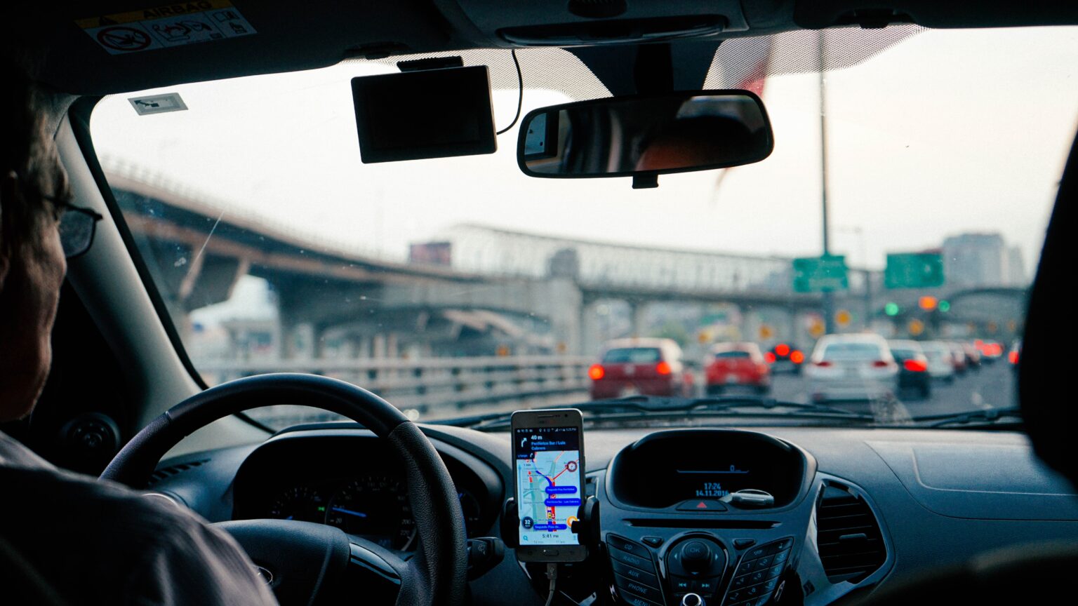 A view of a highway from the backseat of a car with the man driving using his phone as a sat nav