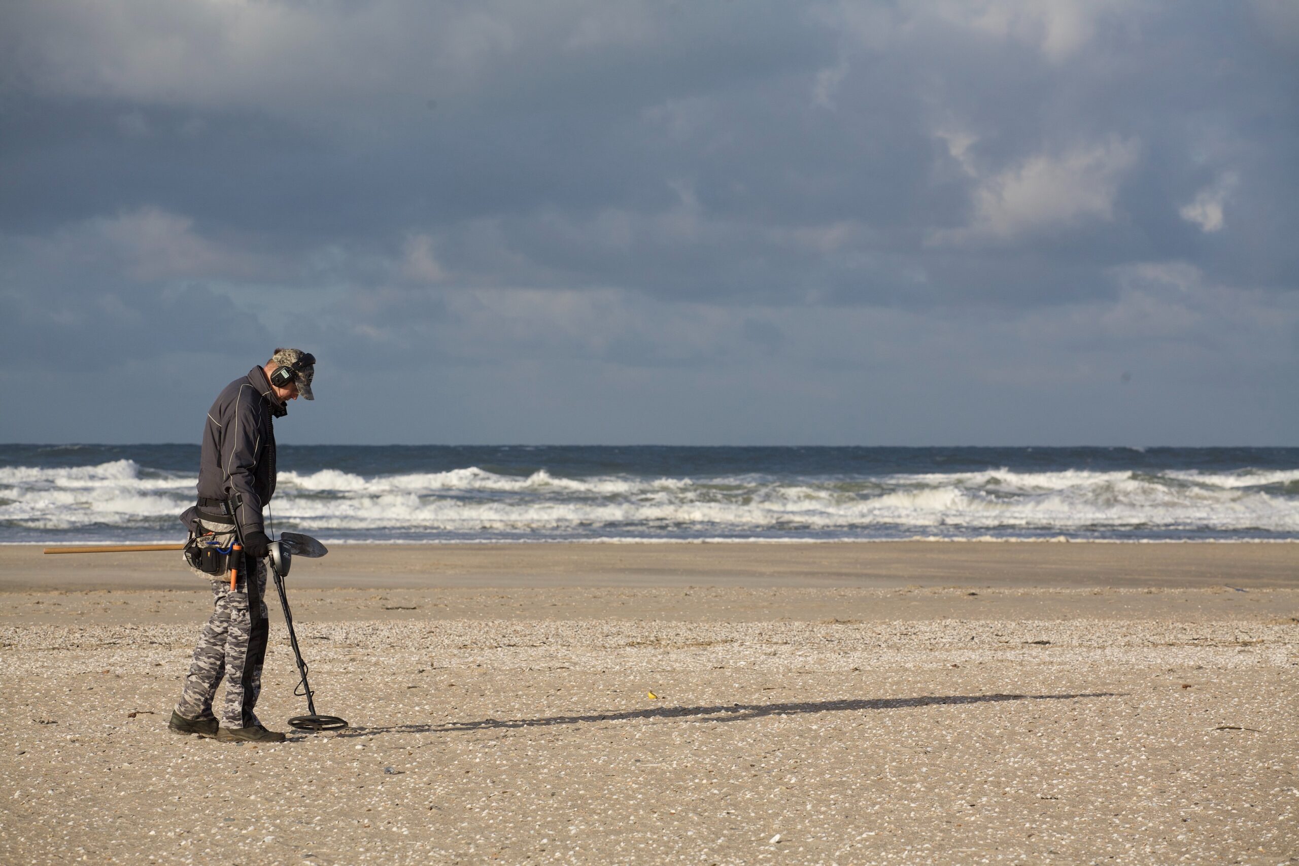 A man using a metal detector on a beach with the sea in the background