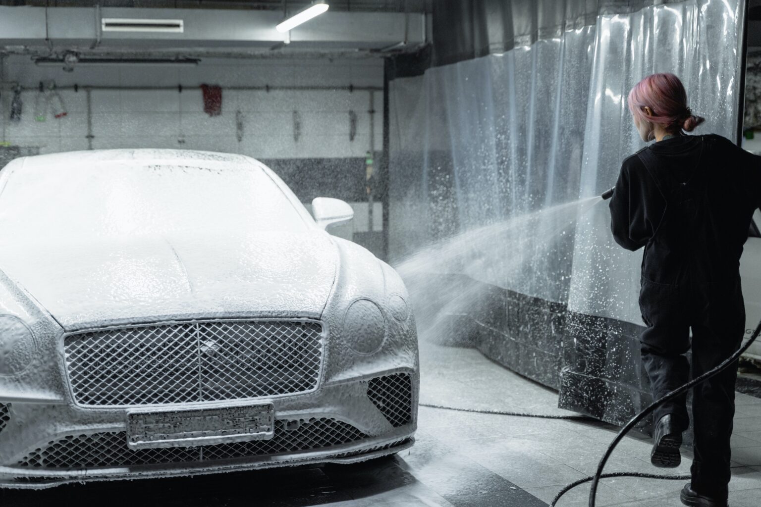 A woman washing a bentley with a Commercial Pressure Washer inside a workshop