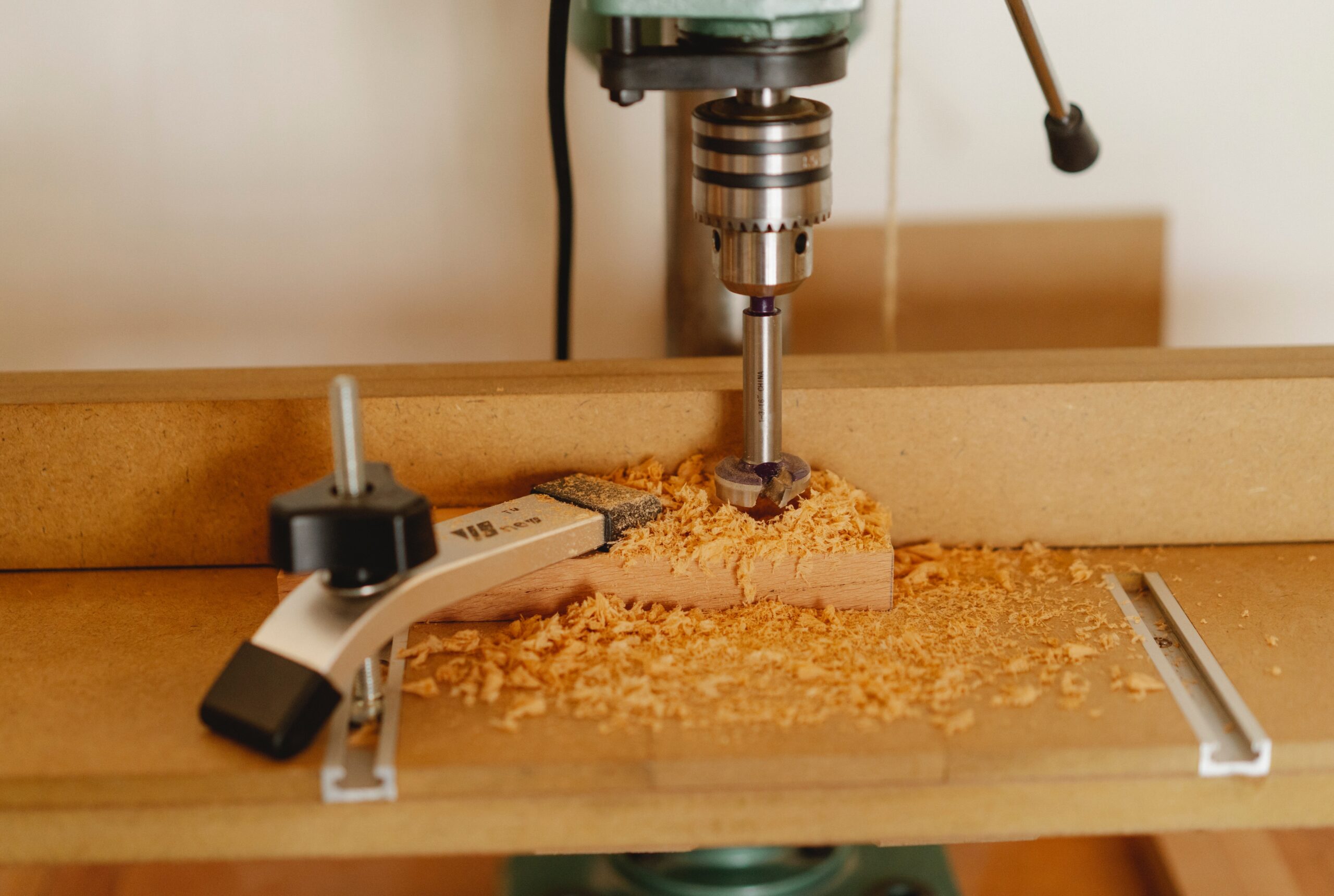 A Pillar Drill drilling a piece of woods with sawdust around it