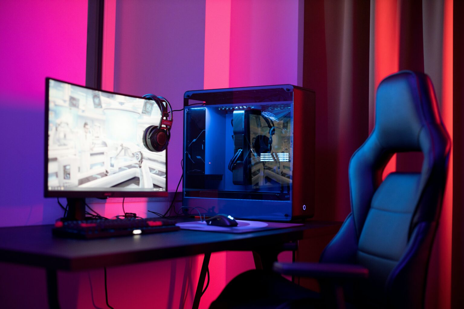 A PC gaming setup with gaming chair surrounding by pick and red LEDs