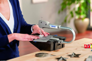 A woman using a Scroll Saw attached to a table to cut a piece of material