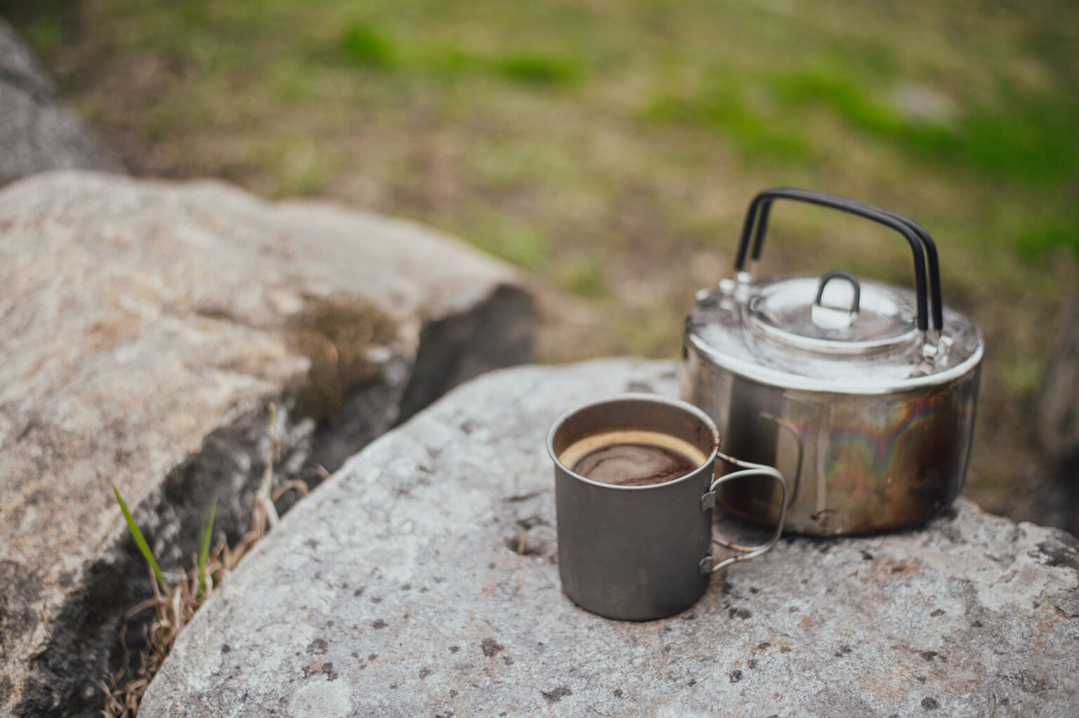 A rock with a travel kettle and a cup of coffee on it