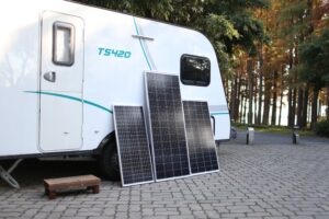 A caravan in the woods with 3 solar panels leaning on it