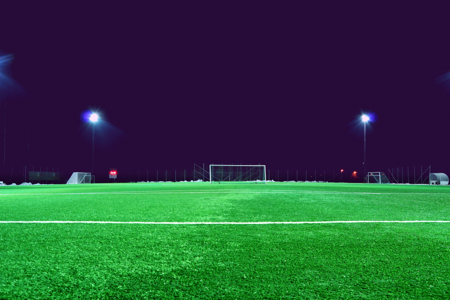 A football pitch at night with artificial grass lit by floodlights