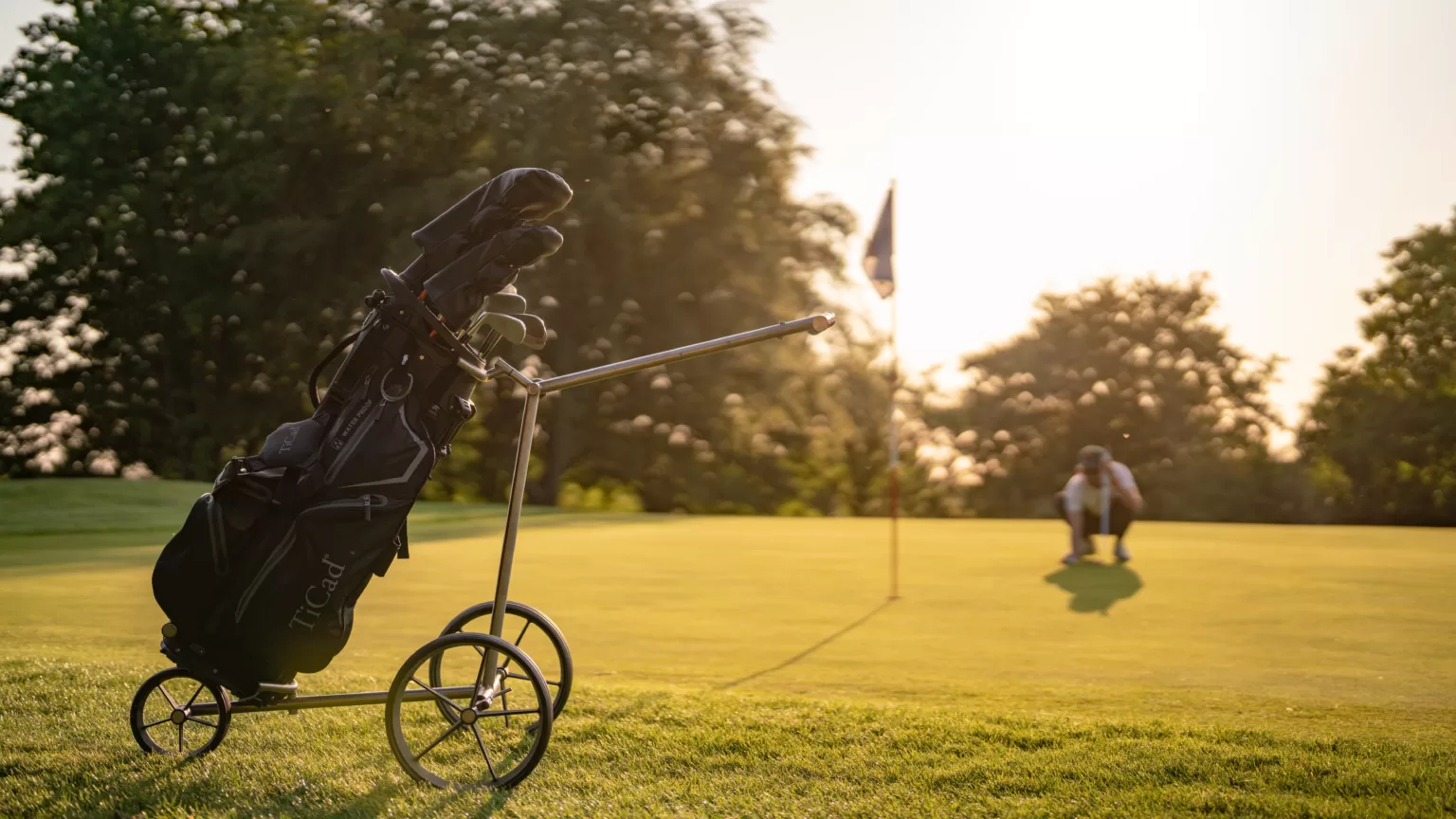 A golf cart on a golf course with a man picking up a golf ball behind it