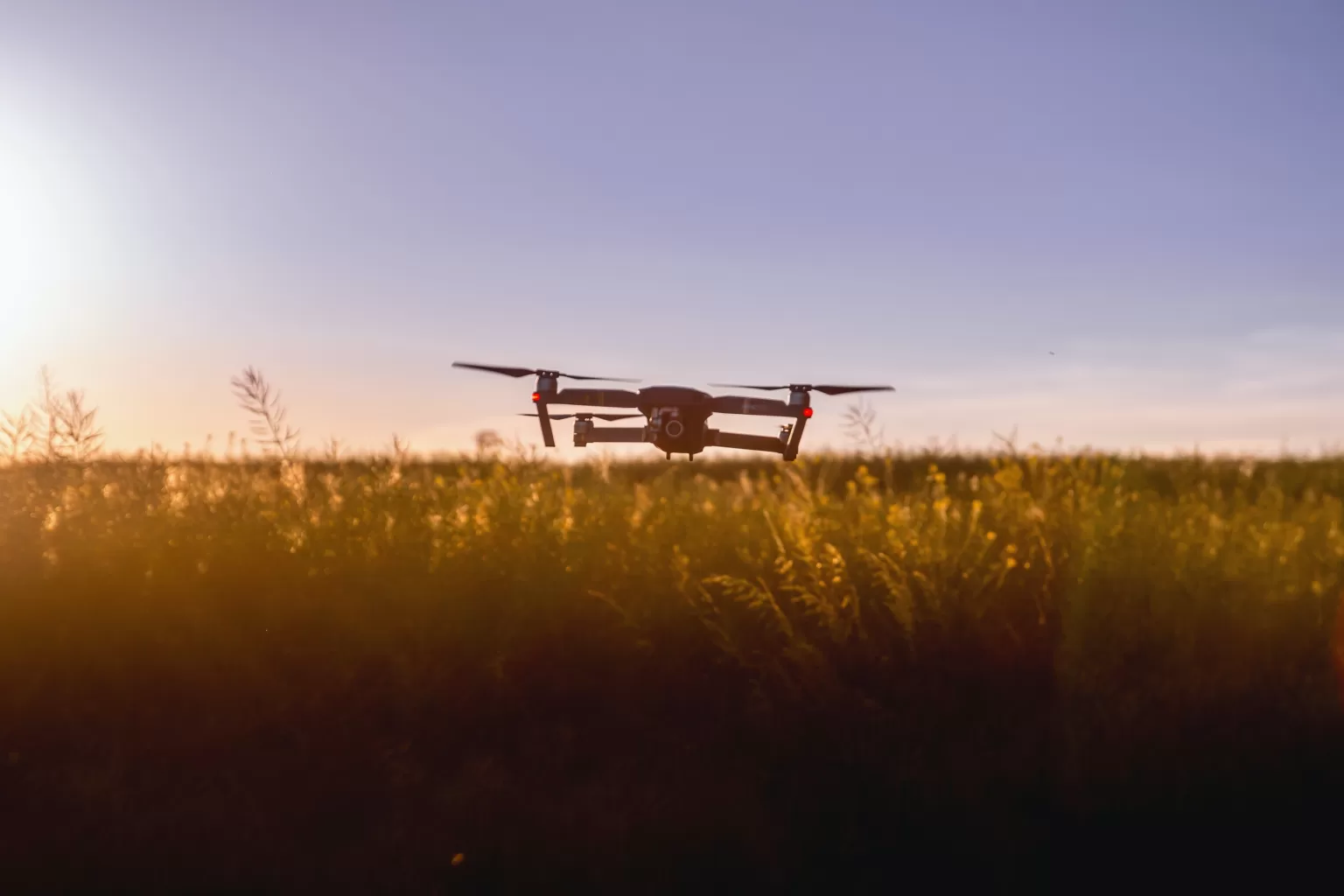 A drone flying over a field with a beautiful sun in the background