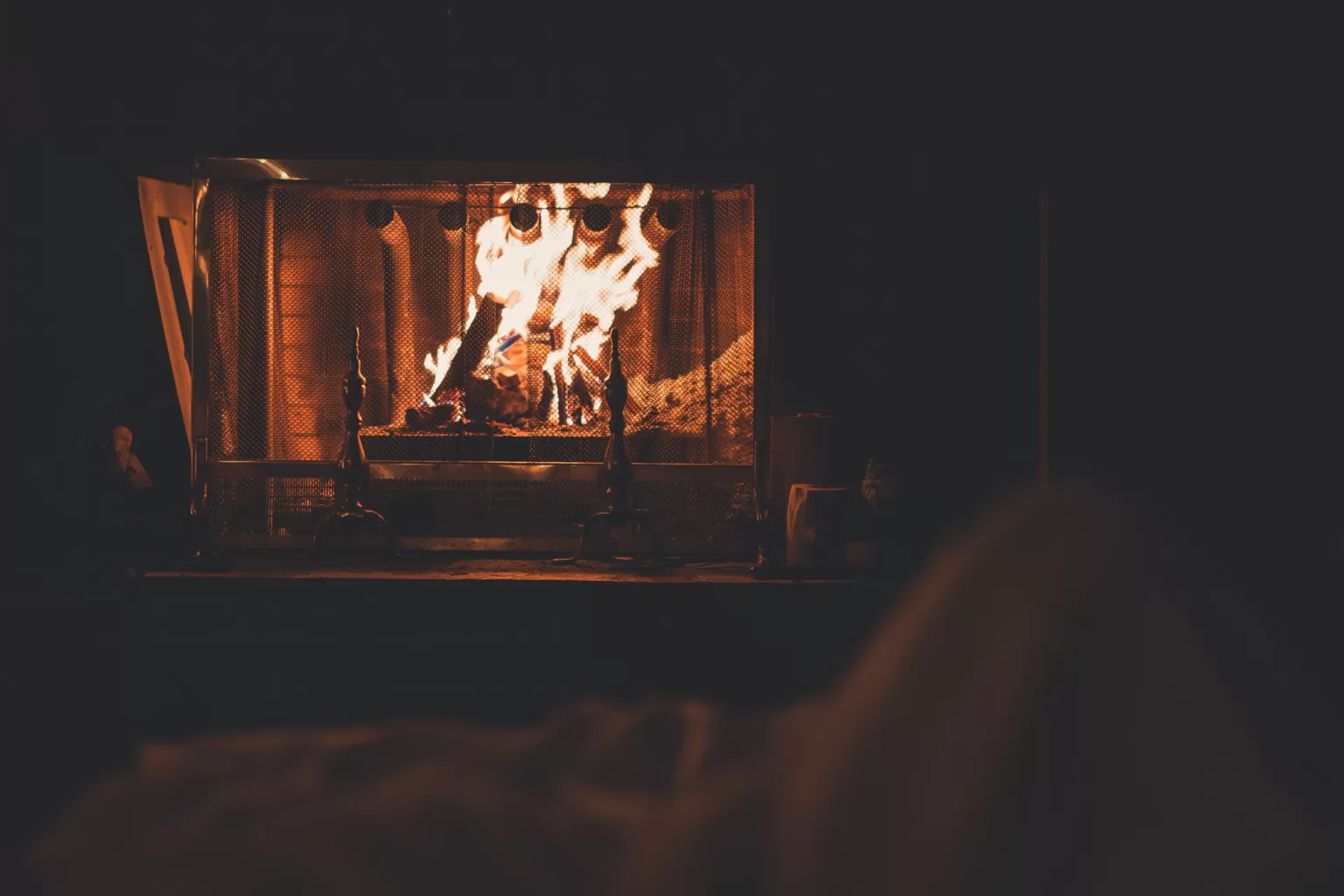 A fire in a living room behind a metal link screen