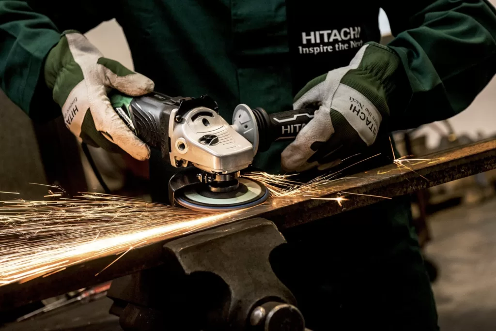 A man using a corded Hitachi Angle Grinder on a piece of metal