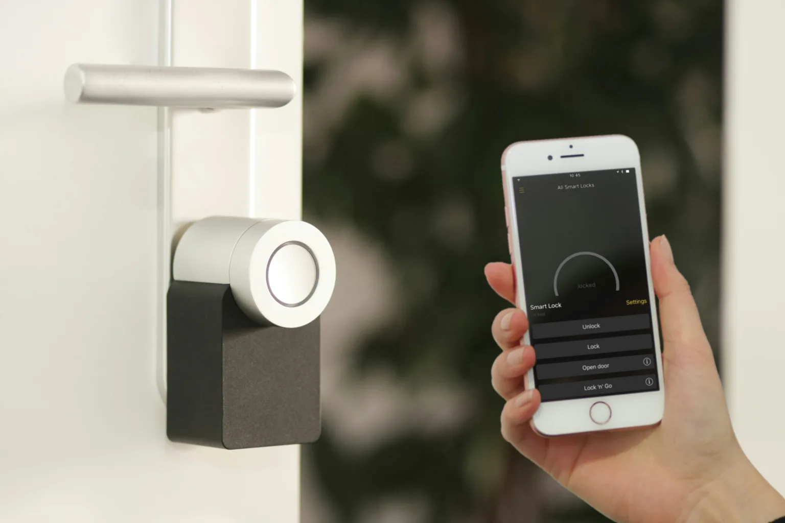 A hand holding a phone with smart lock control options on the screen next to a smart lock on a door