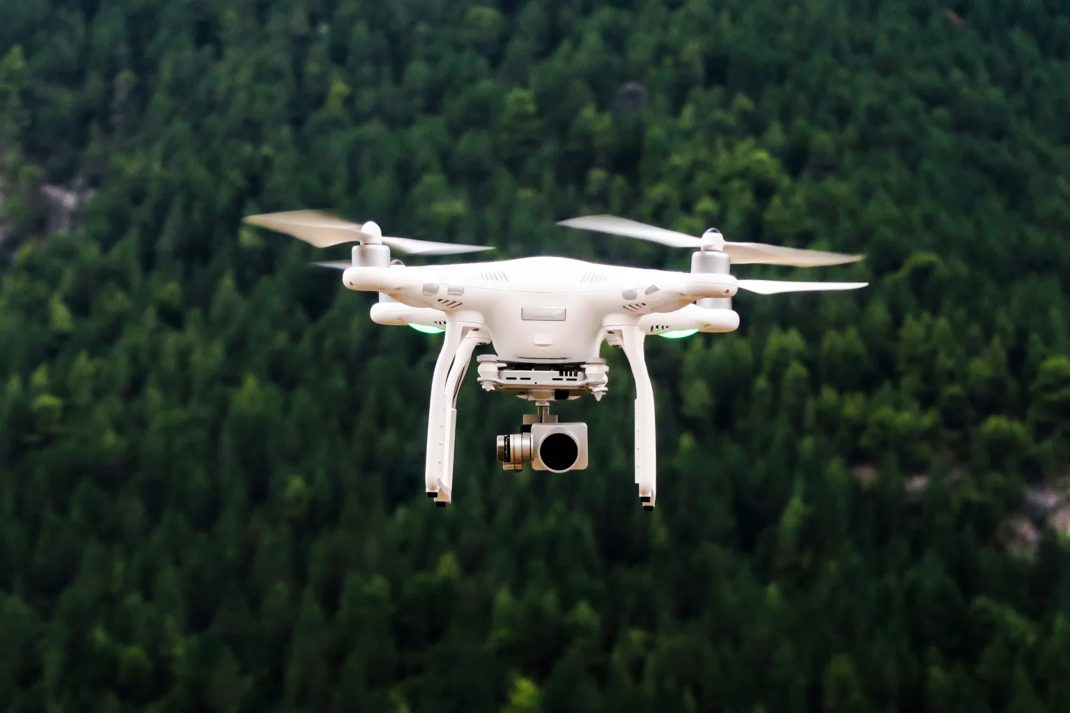 A camera drone flying with a blurred forest behind it