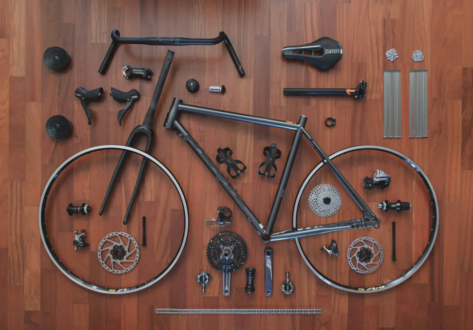 A bike broken down into all of it's basic components on a wooden floor