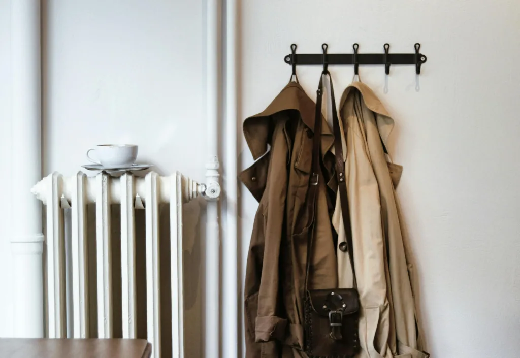 Small white radiator next to some clothes hooks with jackets on them