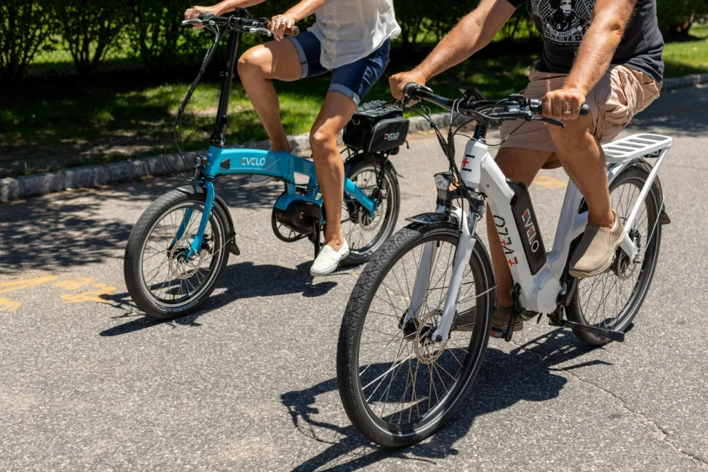 Two people riding electric bikes along a woodland path