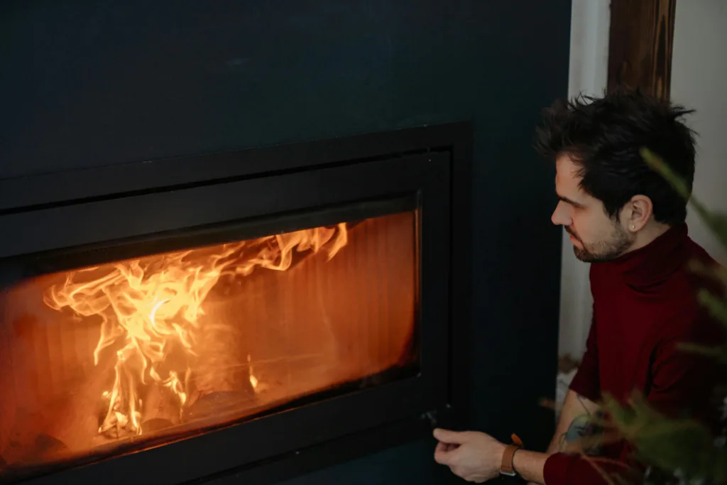 A fire place covered with a grass screen with a man sat next to it