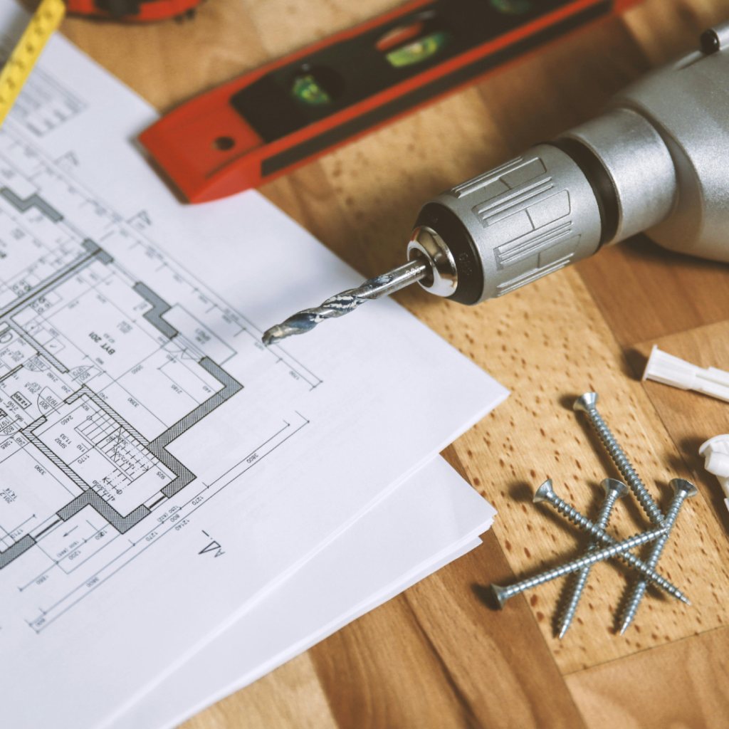 Floorplans, a drill, a level and some screws on a wooden floor