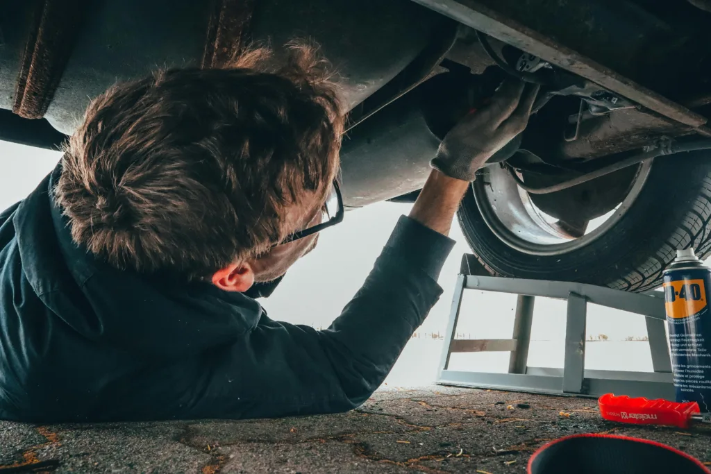 Man working underneath a car next to a can of WD40